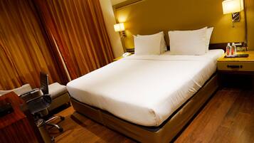 Ein Hotelzimmer mit einem großen Bett, einem Schreibtisch mit Stuhl, einem Nachttisch mit Lampe und einem Fenster mit Vorhängen.