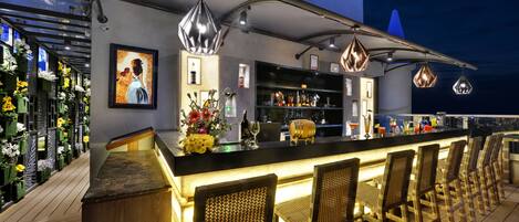 A bar area with wicker chairs, a counter with bottles, and a wall with a framed picture.
