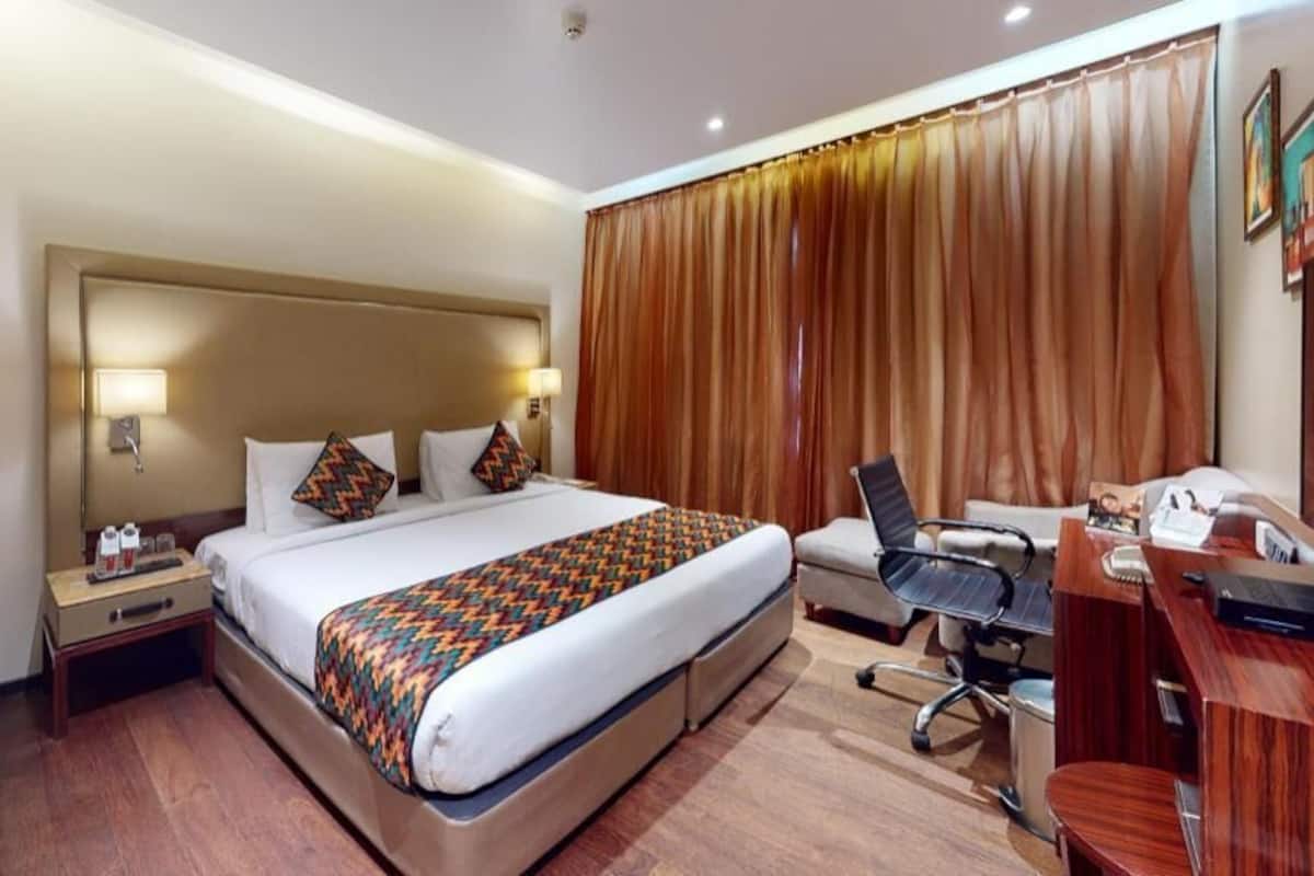 Une chambre d’hôtel avec un grand lit, des lampes de chevet, un bureau avec une chaise et une fenêtre avec des rideaux.