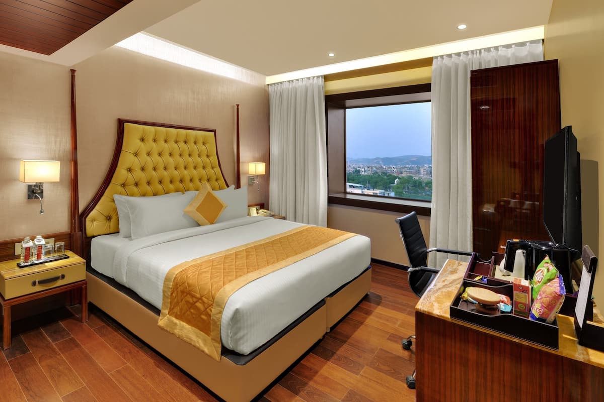Une chambre d’hôtel avec un grand lit, un bureau avec un ordinateur, une télévision et une fenêtre donnant sur la ville.