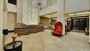 Un hall d’entrée spacieux, agrémenté d’un lustre, d’un comptoir de réception et d’un fauteuil rouge.