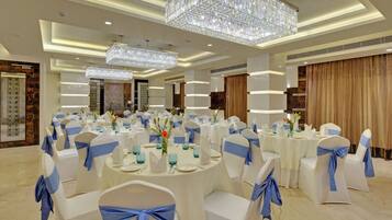 Une salle de banquet avec des tables rondes, des chaises blanches ornées de rubans bleus et un grand lustre en cristal.