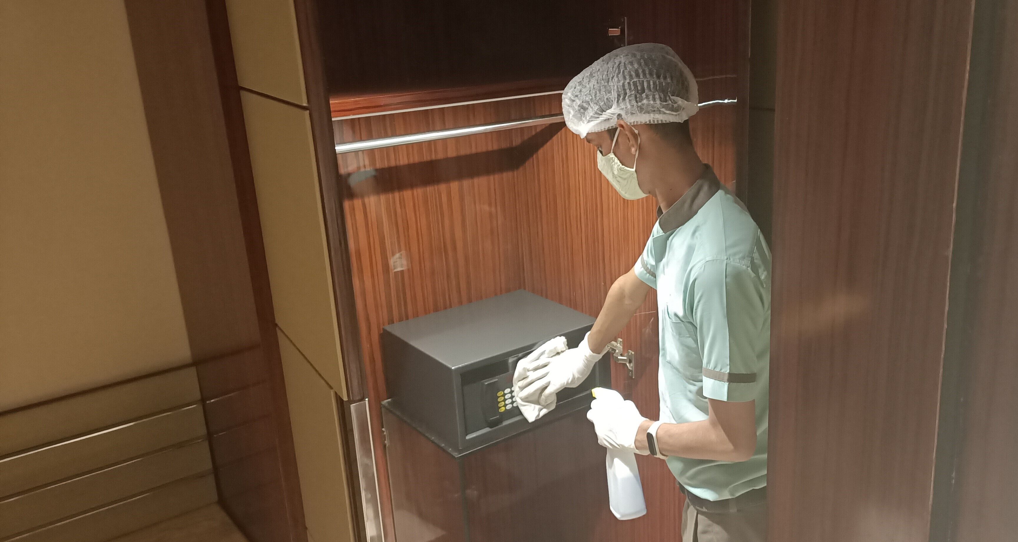 Una persona con uniforme verde limpiando un microondas en una habitación con paneles de madera.