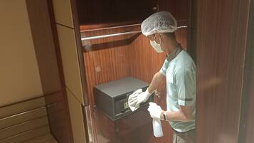 Una persona con uniforme verde limpiando un microondas en una habitación con paneles de madera.