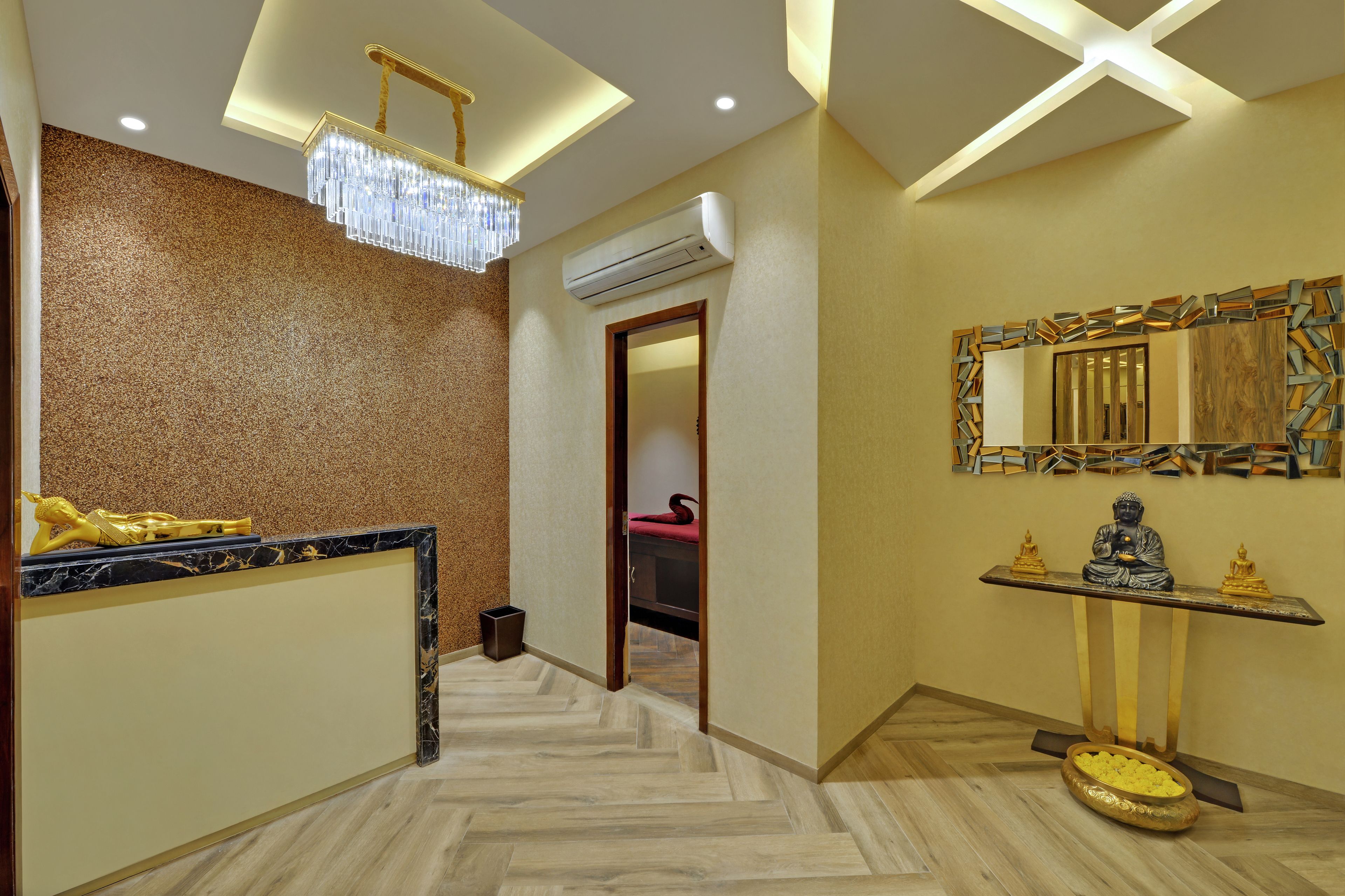 En hotellobby med en receptionsdisk i marmor, en lysekrone, en aircondition-enhed, en Buddha-statue og en dekorativ væg.
