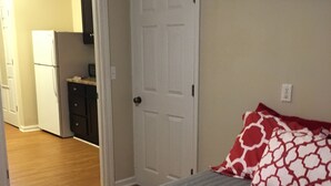 Een slaapkamer met een bed, een deur en een keuken op de achtergrond.