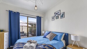 A bedroom with a large bed, a nightstand with a lamp, a dresser, and a view of the outside. - Comfort on Crouch- Enjoy this beautiful house right in CBD.  (Mount Gambier)