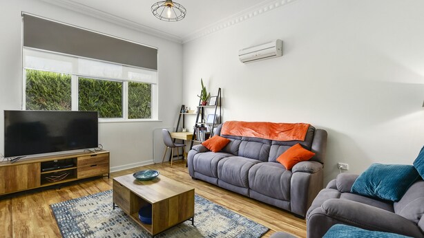 A modern living room with a flat-screen TV, grey sofa, wooden coffee table, and a large window with a view of greenery. - Comfort on Crouch- Enjoy this beautiful house right in CBD.  (Mount Gambier)