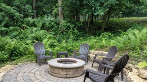 A circular outdoor seating area with a fire pit, surrounded by a paved walkway and lush greenery.