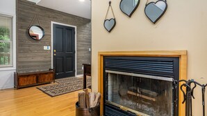 A room with a wooden floor, a black door, a fireplace with a screen, and three heart-shaped mirrors on the wall.