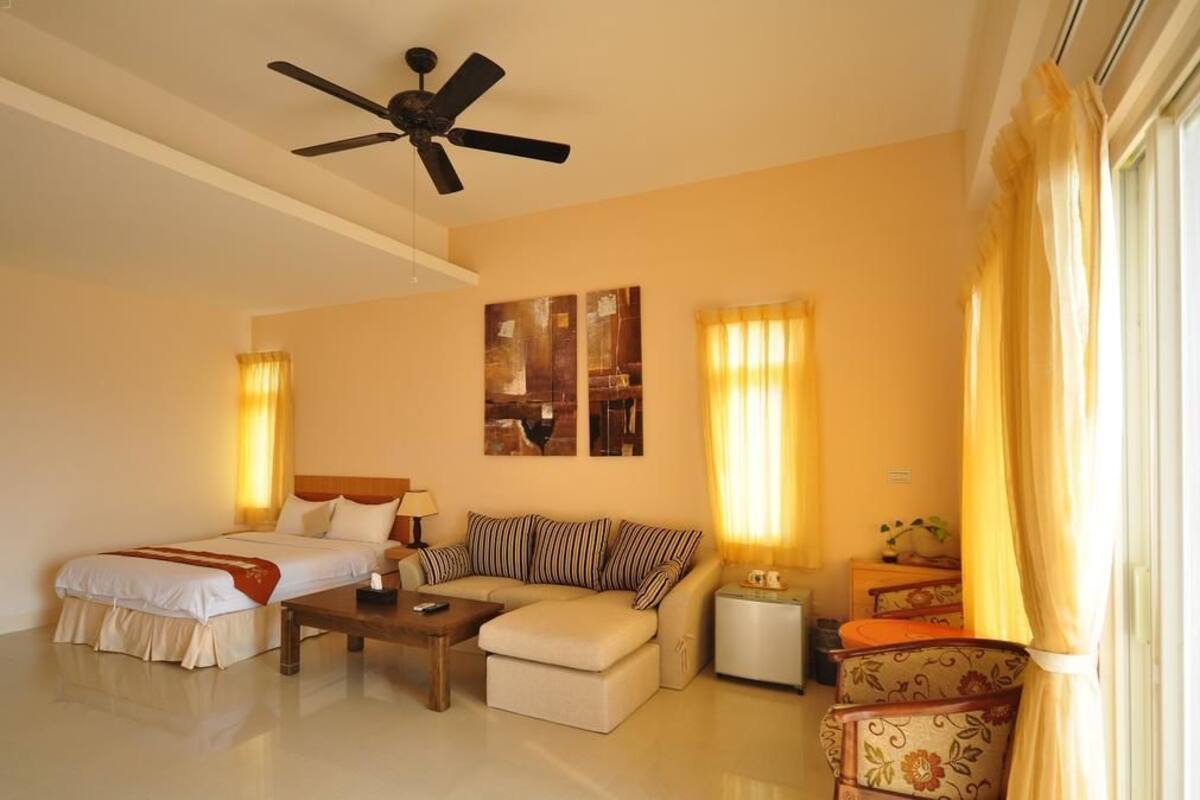 A hotel room with a bed, a sofa, a coffee table, a side table, and a ceiling fan.