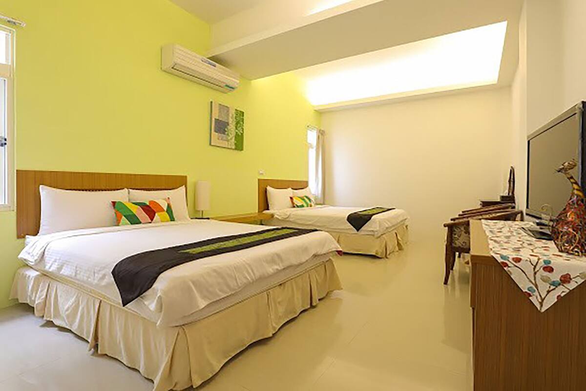 A hotel room with two beds, a desk, a chair, and a large window providing natural light.