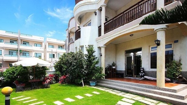 A hotel with a covered entrance, a well-maintained garden, and a multi-story building in the background. - Summer Time B&B (Magong)