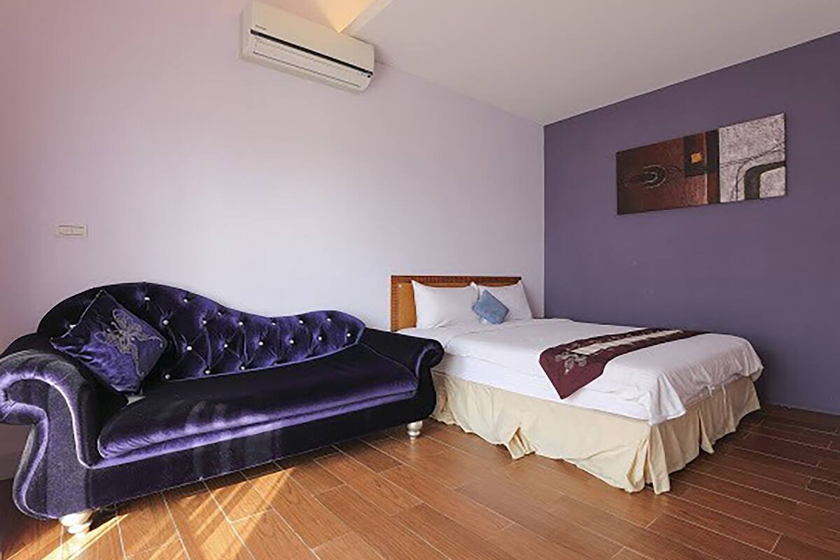 A bedroom with a bed, a sofa, and an air conditioning unit.