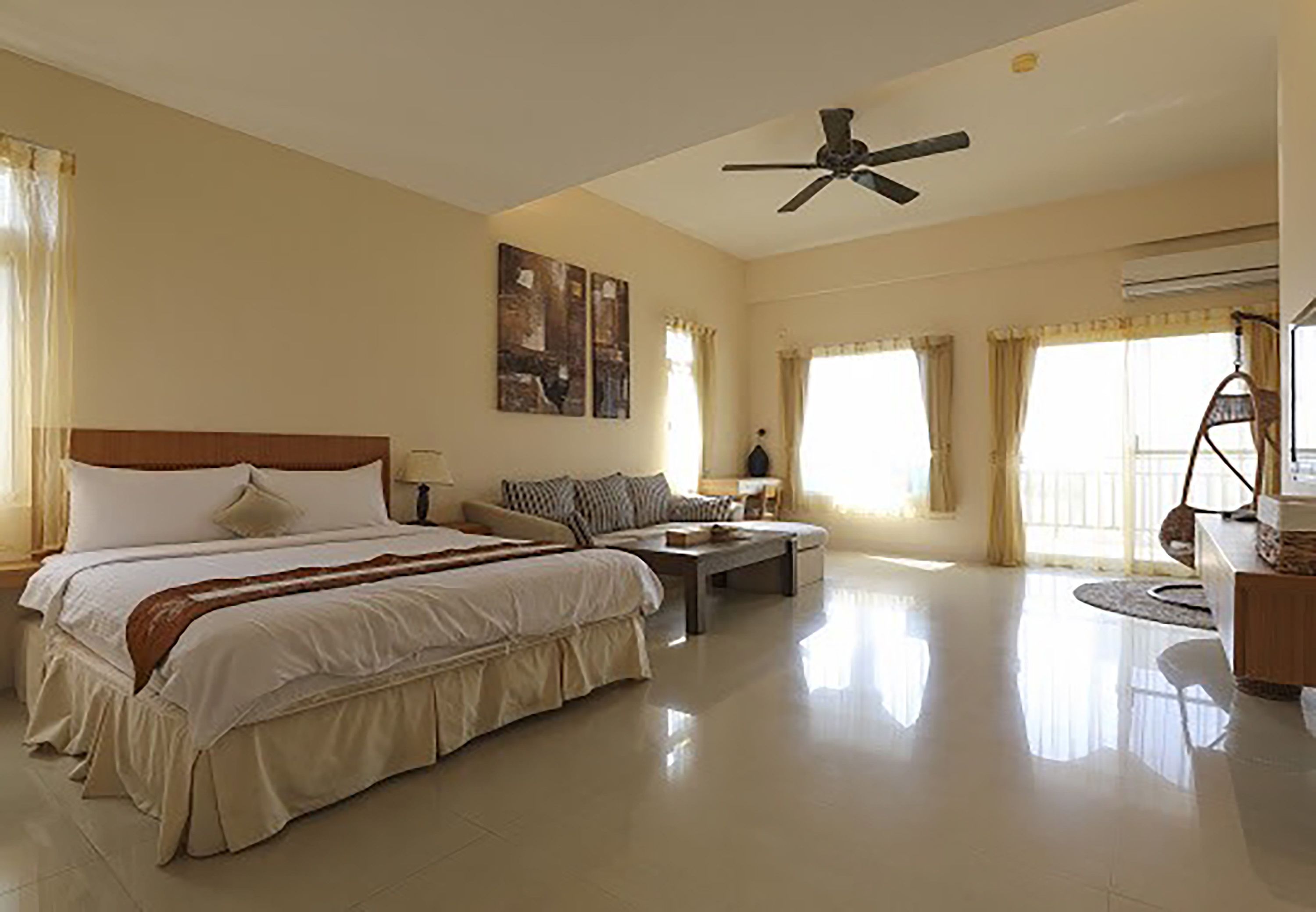 Um quarto de hotel espaçoso com uma cama grande, uma escrivaninha, uma cadeira e um ventilador de teto.