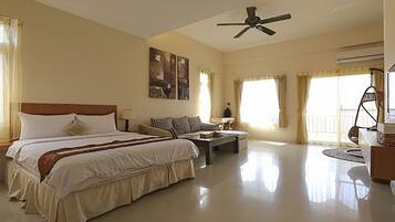Um quarto de hotel espaçoso com uma cama grande, uma escrivaninha, uma cadeira e um ventilador de teto.
