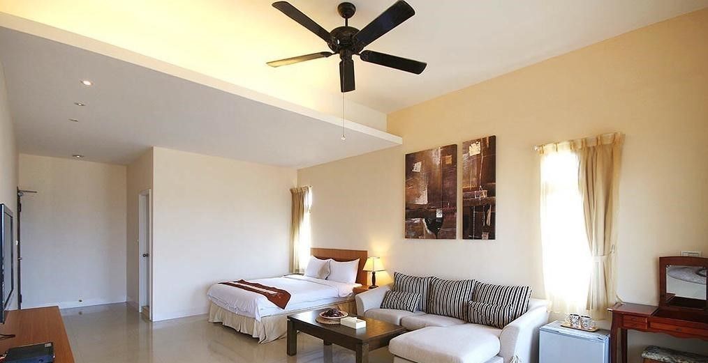 A hotel room with a bed, a sofa, a coffee table, a ceiling fan, and artwork on the wall.