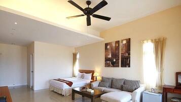 A hotel room with a bed, a sofa, a coffee table, a ceiling fan, and artwork on the wall.