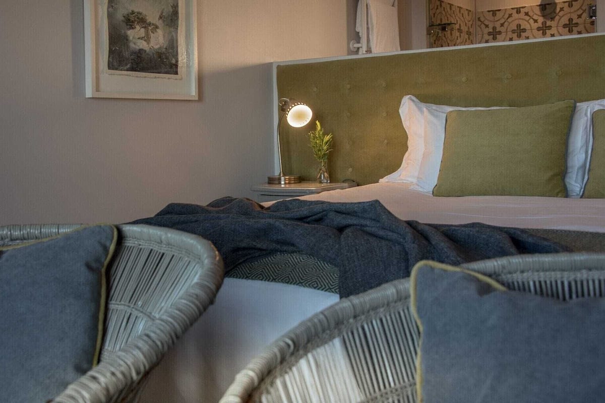 A hotel room with a bed, a bedside lamp, a framed picture on the wall, and a window with a view.