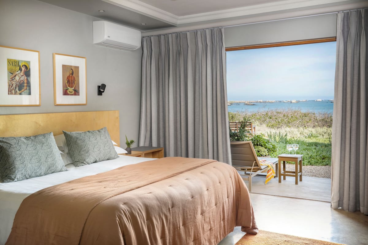A bedroom with a large bed, a nightstand, a chair, and a view of the sea.
