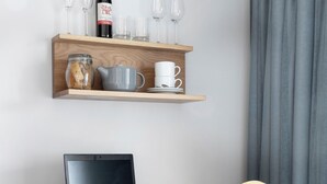 Een houten bureau met een laptop, een houten stoel, een plank met wijnglazen, een wijnfles en een koffiekop.
