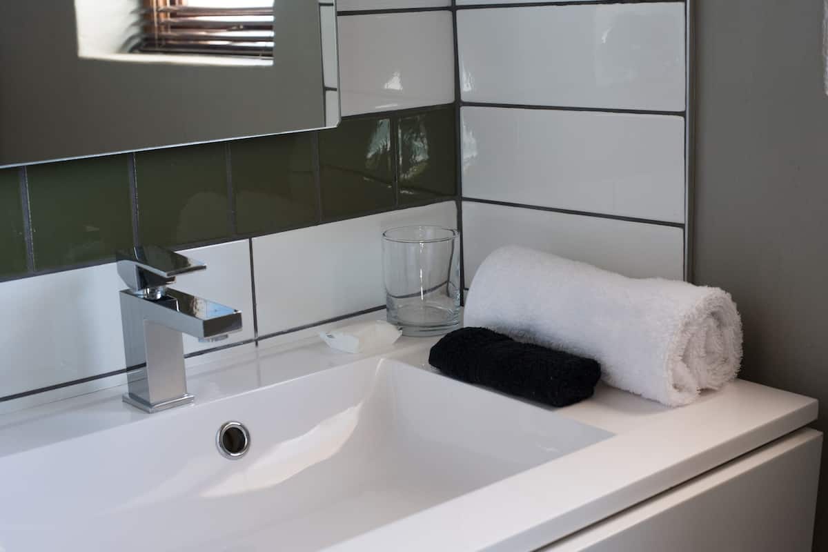 A bathroom with a white sink, a mirror, a towel, and a glass.
