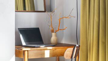 Un escritorio de madera con una laptop, un florero con ramas, una silla, una lámpara de escritorio y un espejo.
