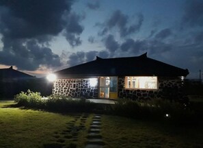 Ein Steinhäuschen mit Veranda und einem Weg, der davor führt, unter bewölktem Himmel.