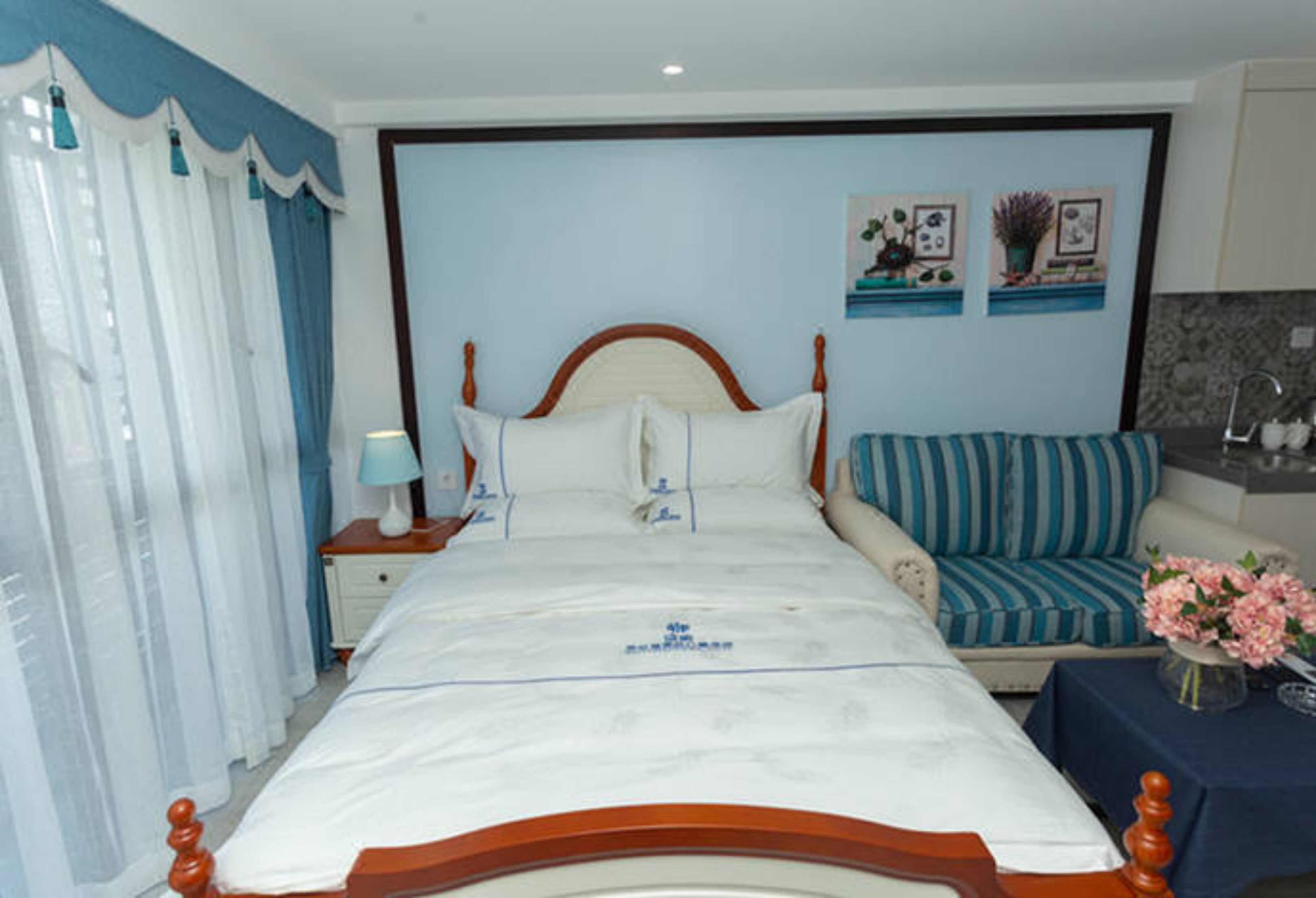 A bedroom with a bed, a nightstand, a blue-striped sofa, and a small table with a vase of flowers.