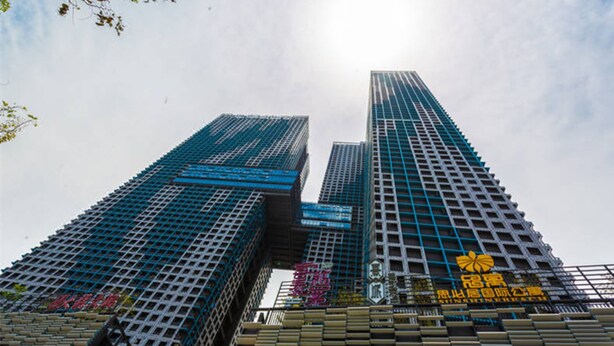 Dois edifícios altos com fachada em grade, um com tom azul e outro com um letreiro amarelo.