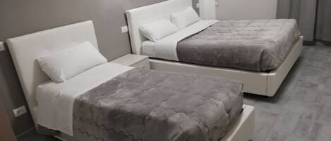 Une chambre d’hôtel avec deux lits, chacun doté d’une tête de lit blanche et d’une couvre-lit matelassée grise. Deux appliques murales sont fixées au-dessus de chaque lit.