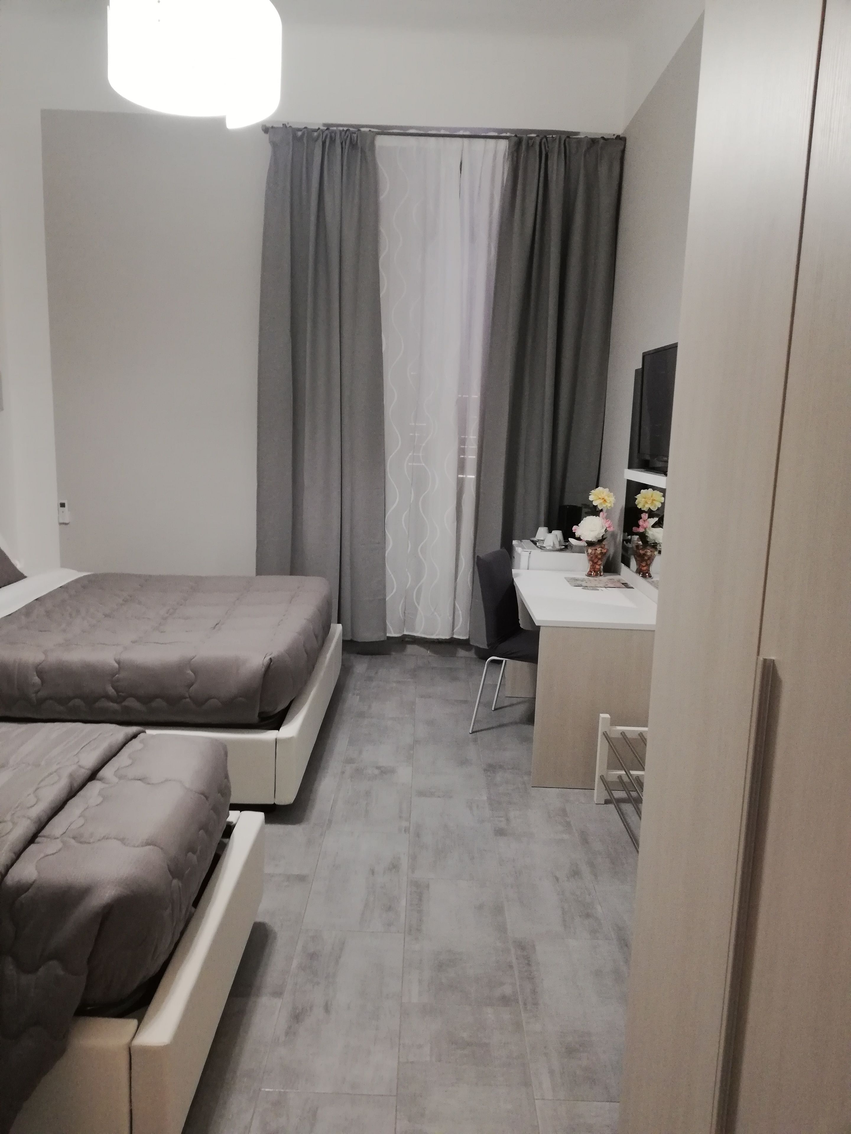 Une chambre avec deux lits, un bureau, une chaise, un miroir et une fenêtre avec des rideaux.