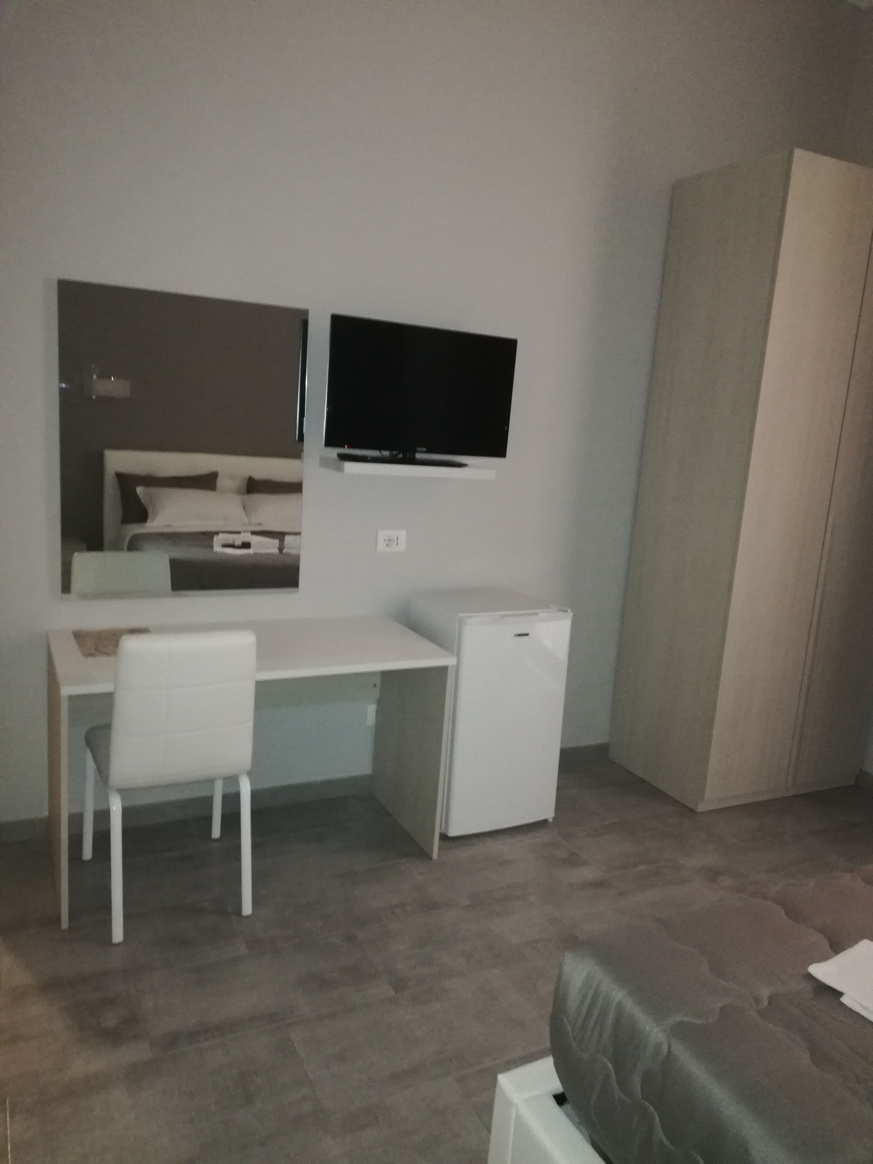 A bedroom with a bed, a desk with a chair, a TV, and a wardrobe.