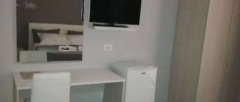 A bedroom with a bed, a desk with a chair, a TV, and a wardrobe.