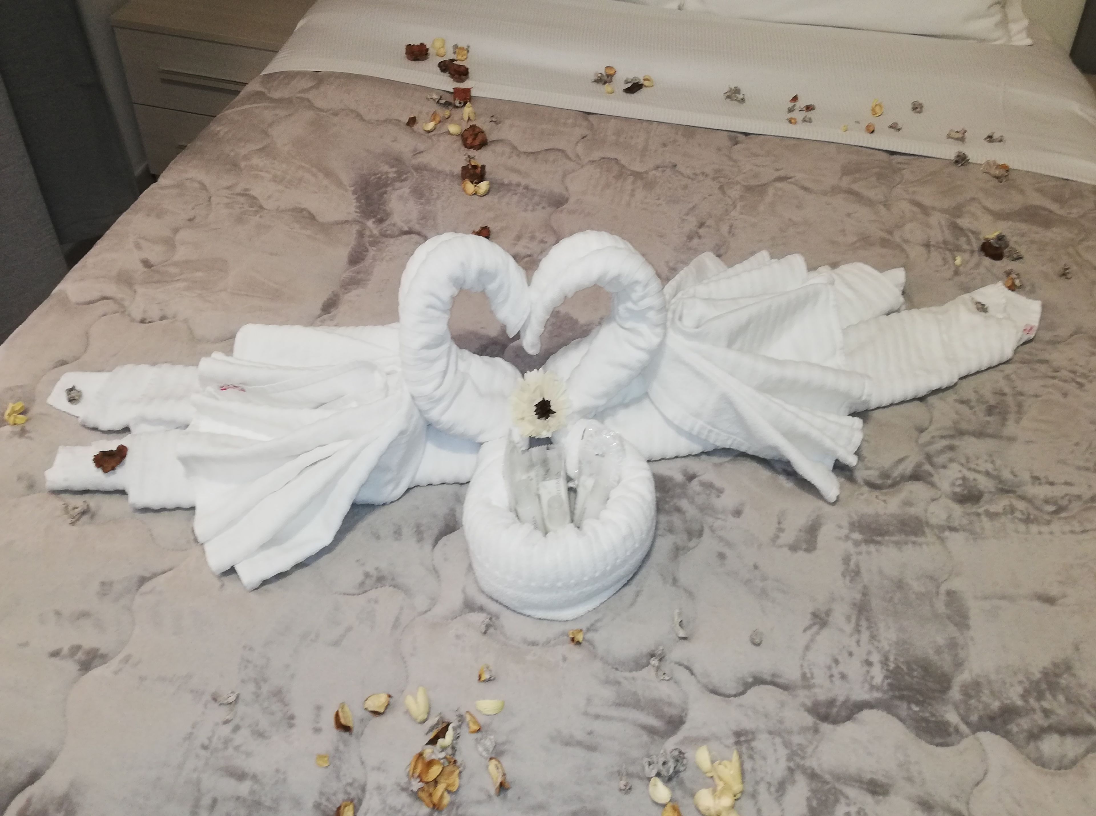 A bed with a towel arranged in the shape of a swan, placed on a marble-patterned bedspread.
