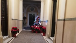 Un couloir décoré d’un sapin de Noël et de quelques poinsettias, qui mène à une porte dotée d’une fenêtre ronde.