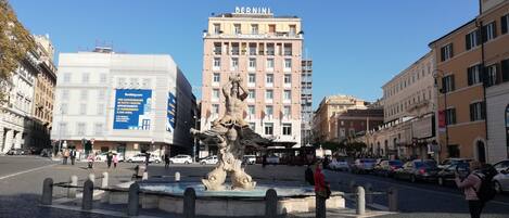 A public square with a fountain, surrounded by historic buildings and a hotel with a large sign.