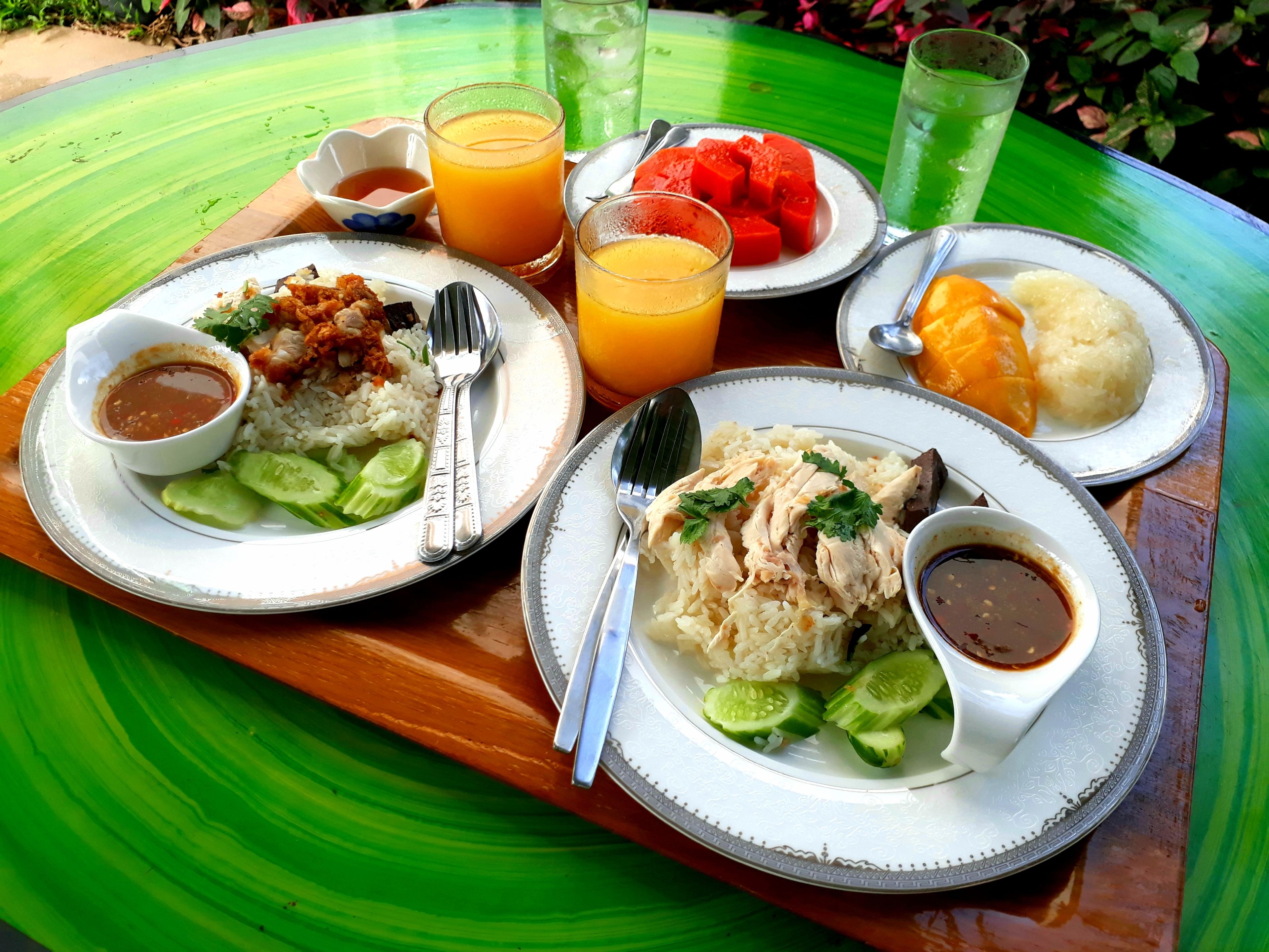 Une table dressée avec des assiettes remplies de nourriture, notamment du riz, du poulet et des légumes, accompagnée de boissons et de condiments.