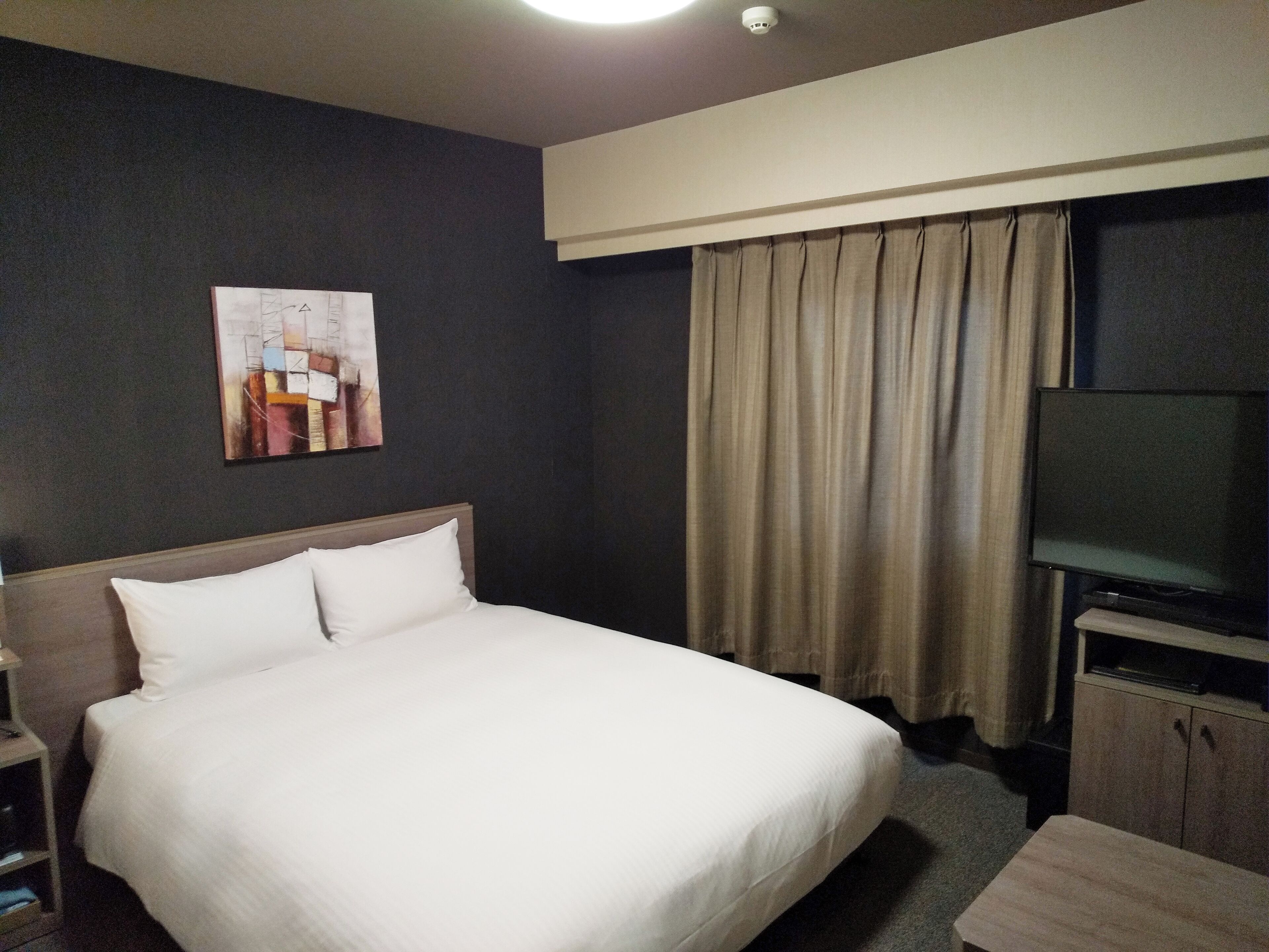 A hotel room with a large bed, a flat-screen TV, a wooden headboard, a small table, and a painting on the wall.