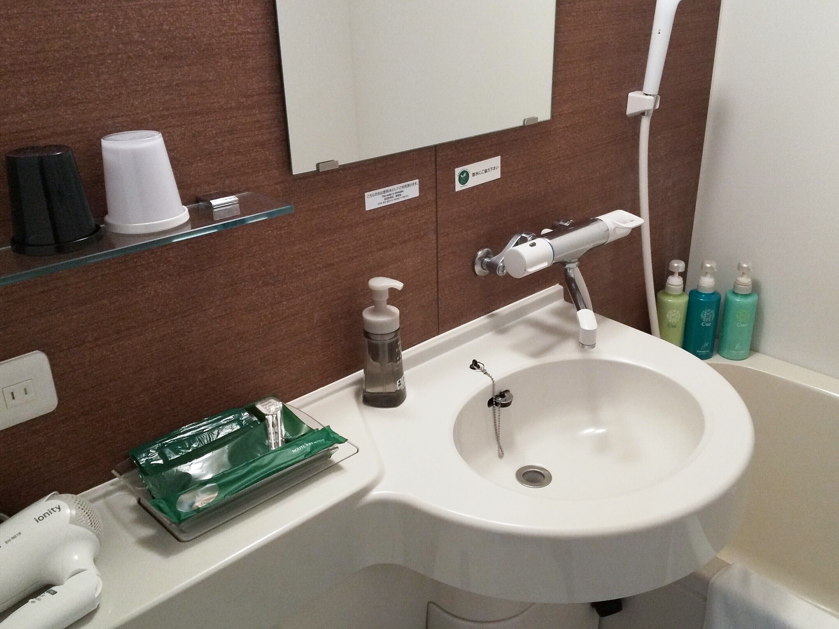 Een badkamer met een witte wastafel, een spiegel, een handdoekdispenser en toiletartikelen aan de muur.