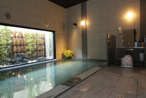 A spa pool with a view of bamboo and rocks, a small flower arrangement, and a shower area with a toilet. - Hotel Route Inn Ishioka (Ishioka)