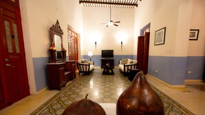 A room with a patterned floor, a television, two chairs, a sofa, a wooden cabinet, and a red door. - Style and luxury in the heart of El Centro (Merida)