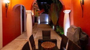 A corridor with a covered seating area, white columns, and a bright orange wall. - Style and luxury in the heart of El Centro (Merida)