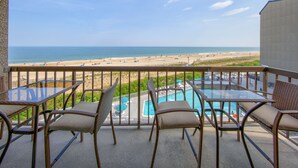 Un balcon meublé avec des meubles en osier, donnant sur une plage et une piscine.