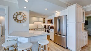 Une cuisine moderne avec des meubles blancs, un grand îlot central doté de tabourets, des appareils en acier inoxydable et une horloge murale.