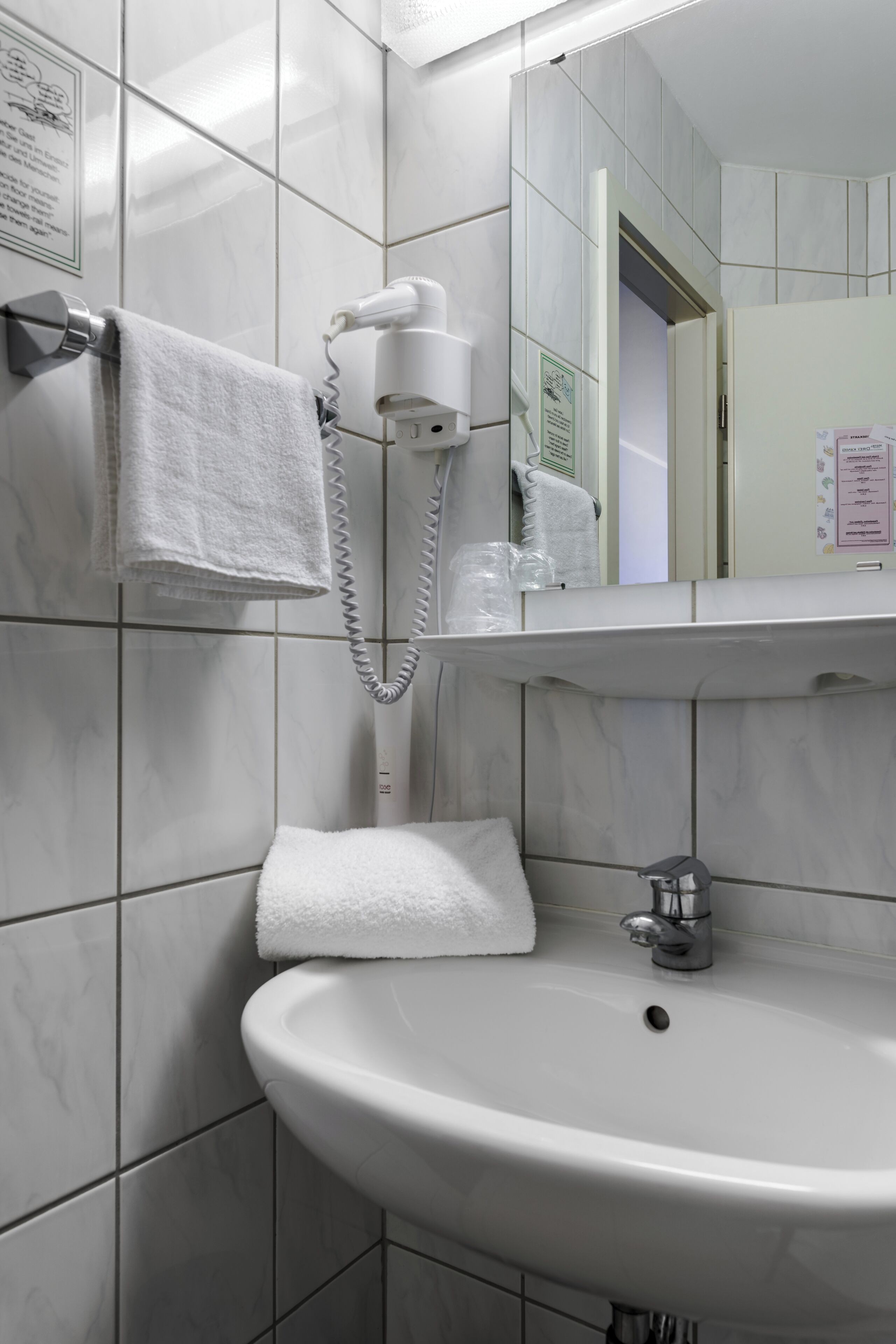 A bathroom with a white sink, a towel rack with a towel, a hairdryer, and a mirror above the sink.