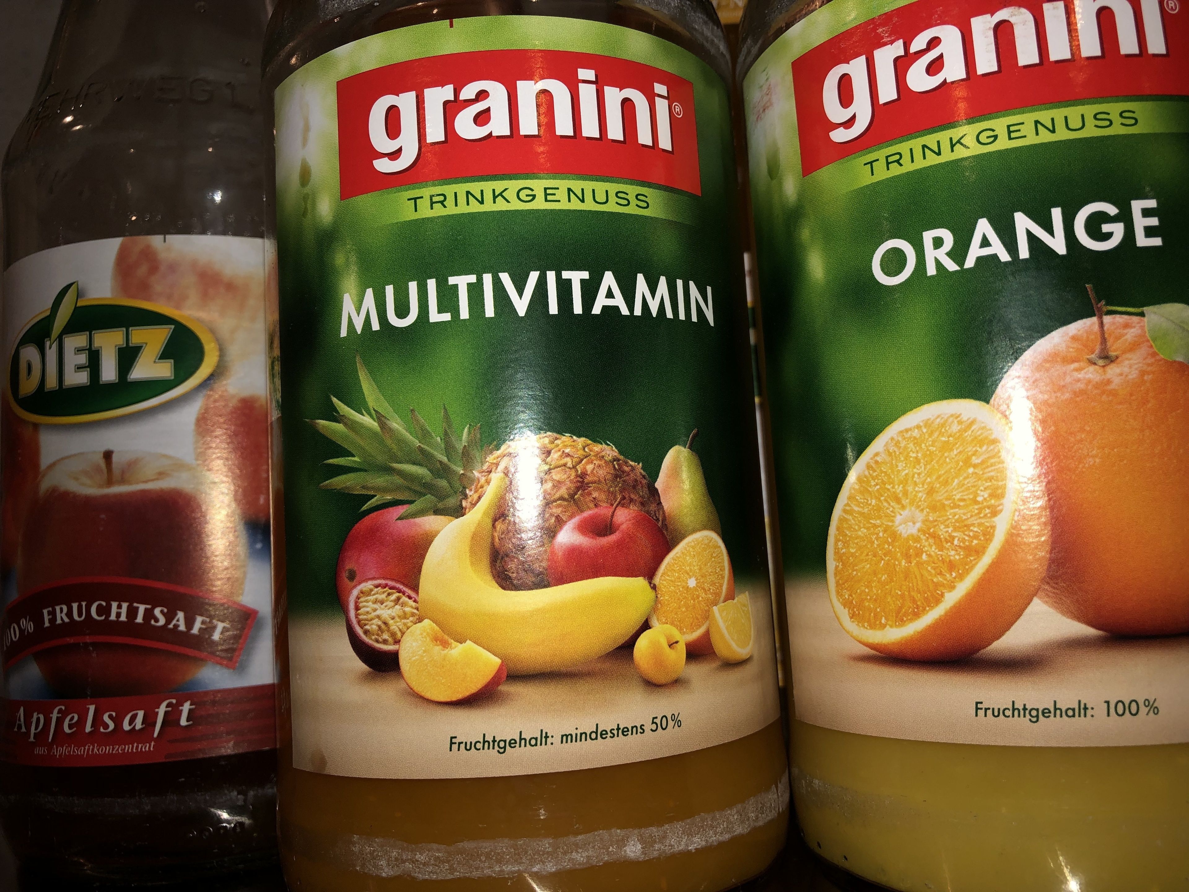 Tres botellas de jugo de frutas Granini, una etiquetada como multivitamínico y la otra de naranja, con imágenes de frutas visibles en las etiquetas.