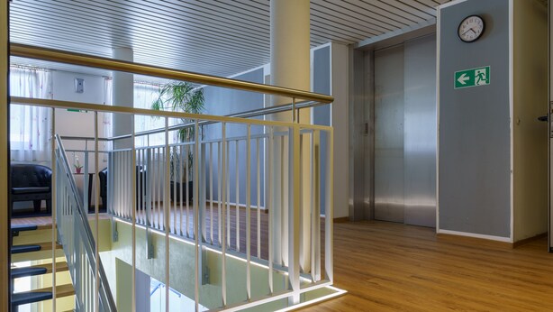 A modern interior with a glass railing, wooden flooring, and an elevator. - Motel Drei König (Heimsheim)