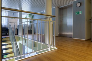 Un interior moderno con barandilla de vidrio, piso de madera y un ascensor.
