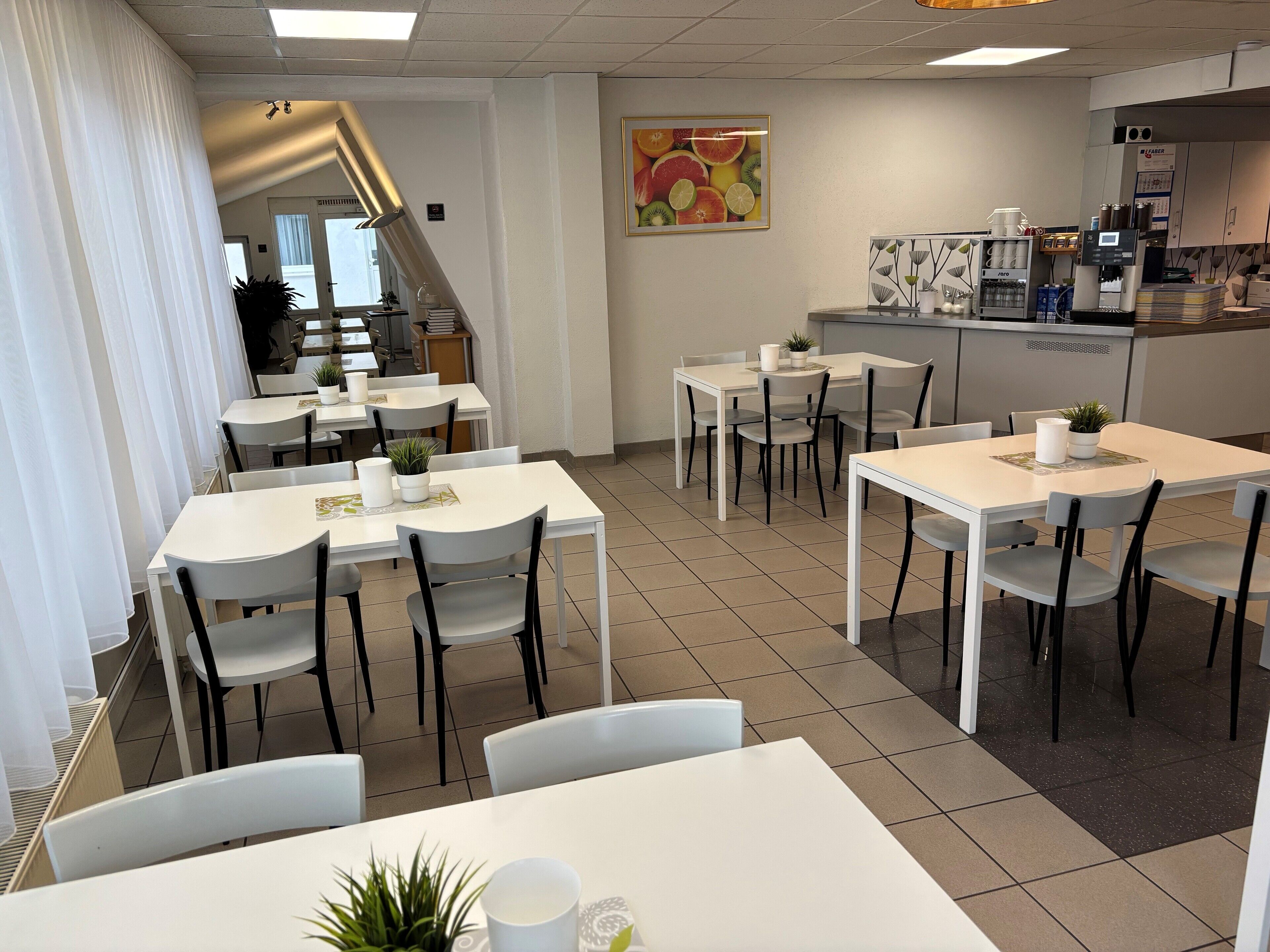 A modern cafe with white tables and chairs, a coffee machine, and a fruit-themed wall art.